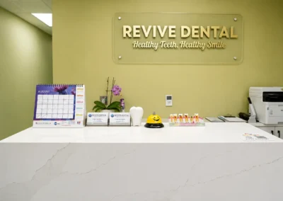 Revive Dental Clinic Front Desk at Revive Dental Mississauga featuring a modern white reception counter, dental models, patient information materials, and Revive Dental wall signage.